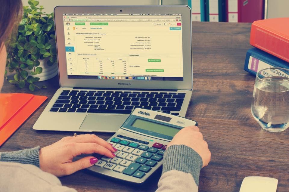 Hands working a calculator next to a laptop while reviewing numbers