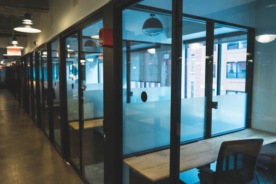 A modern glass-walled office corridor with meeting rooms