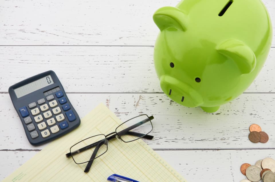 A piggy bank next to a calculator, glasses, and a notepad